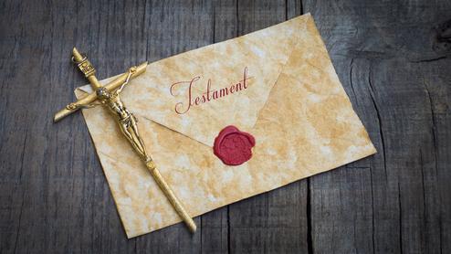 Goldene Kreuzfigur auf einem alten Testamentbriefumschlag mit rotem Wachsiegel auf einer Holzoberfläche.